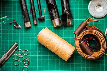 Leather crafting tools make camera strap still life on green wor