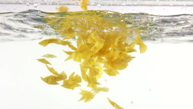Slow motion Italian farfalle pasta falling into water on white background