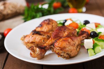 Appetizing oven baked golden chicken drumsticks and Greek salad