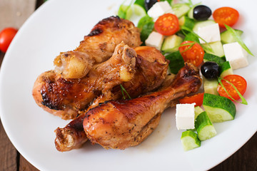 Appetizing oven baked golden chicken drumsticks and Greek salad