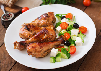 Appetizing oven baked golden chicken drumsticks and Greek salad