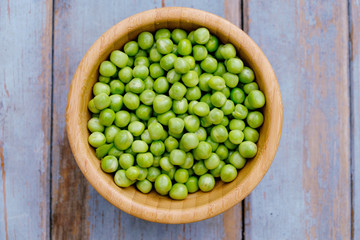 Peas in wooden bowl on wooden background, top view.