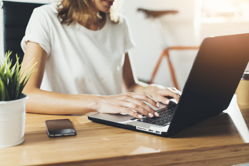Close-up image of young professional female manager using laptop at her office, businesswoman working from home via portable computer, hipster girl freelancer writing on keyboard, flare light