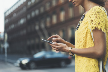 Cropped image of female hands using modern smart phone outside, young hipster girl typing text message in internet via cellphone outdoors, film effects