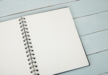 A blank, spiral bound journal on a painted wooden desktop background