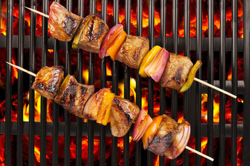 Top view of red meat skewers being grilled in a barbecue.