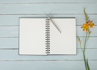 A journal open on a blank page, with flowers and a pen on a blue wooden desktop background