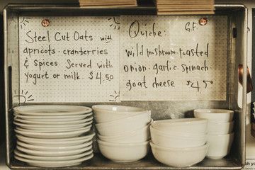 Two menu items written on card. Stacks of plates and bowls. 