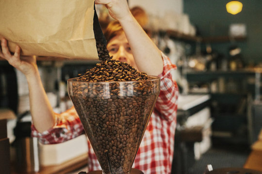 A woman pouring coffee beans into a grinder hopper in a coffee shop. 