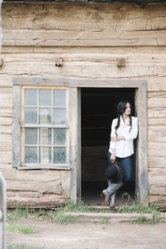 Young woman with long brown hair in braids, standing in the doorway of a wooden cabin.