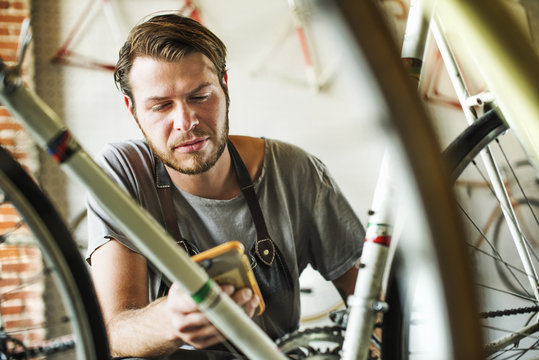 A man working in a bicycle repair shop, checking his smart phone. 