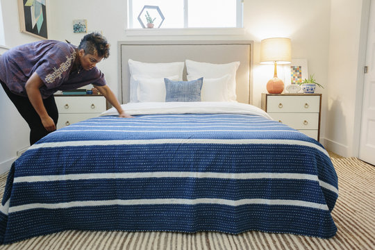 A woman smoothing a blue striped throw over a double bed in a bedroom.  