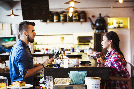 Specialist coffee shop. A man behind the counter using a touch screen to record transactions, and a woman customer. 