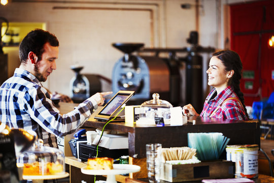 Specialist coffee shop. A man behind the counter using a touch screen to record transactions, and a woman customer. 