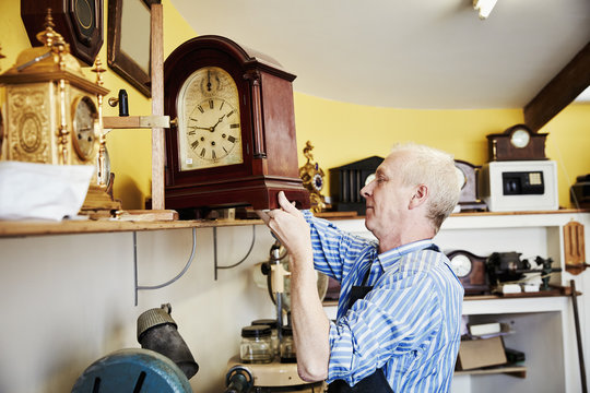 A clock maker displaying his work on a shelf in his workshop.