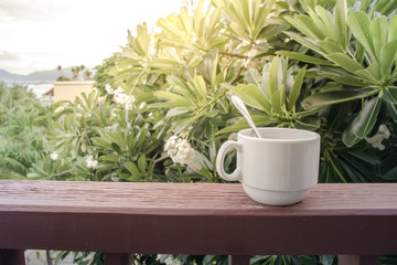 Coffee cup with coffee spoon on the wooden balcony with sunlight in the morning and nature...