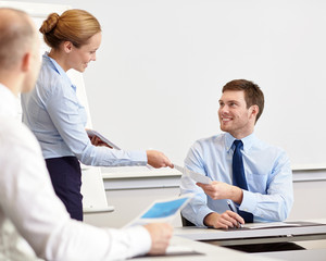 Obraz premium smiling woman giving papers to man in office