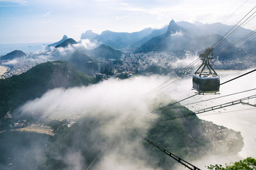 Bright misty view of the city skyline of Rio de Janeiro, Brazil with a Sugarloaf (Pao de Acucar) Mountain cable car passing in the foreground © lazyllama