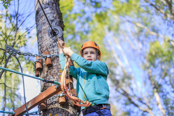 boy struggling with fear of heights. Ziplining. child intends to go through an obstacle course in a...