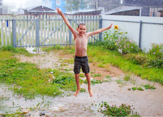 a smiling boy jumping and having fun in summer rain. happy child during the warm summer rain. wet...