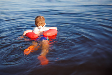 baby swims in the sea with inflatable circle. the boy wearing a modern neoprene shoes for swimming....