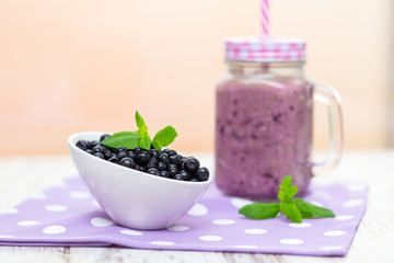 Blueberry smoothie in a glass jar with a straw and bowl of fresh berries