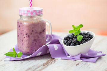 Blueberry smoothie in a glass jar with a straw and bowl of fresh berries