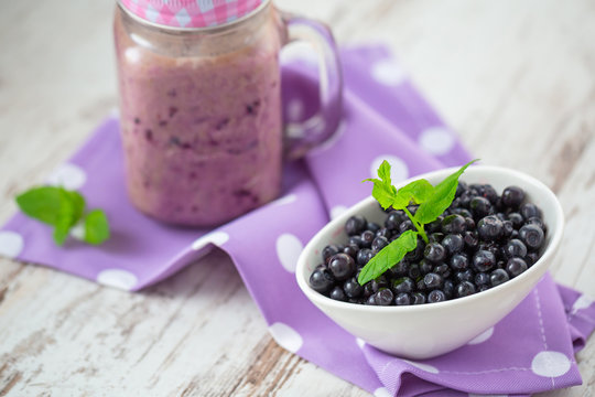 Blueberry smoothie in a glass jar with a straw and bowl of fresh berries