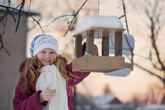 Happy Child Girl With Bird Feeder In Winter Garden