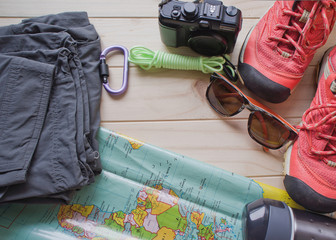 Top view of travel accessories for a mountain trip on old wooden background : hiking boots, pants, camera, bottle, rope, map, notebook and sunglasses.