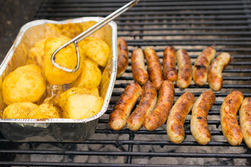 Sausage, hot dogs and potatoes on grill