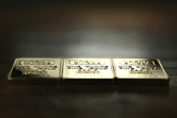 three 1 ounce gold ingots on wooden background