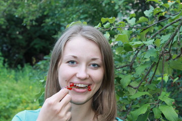 Девушка блондинка ест красную смородину в летнем саду