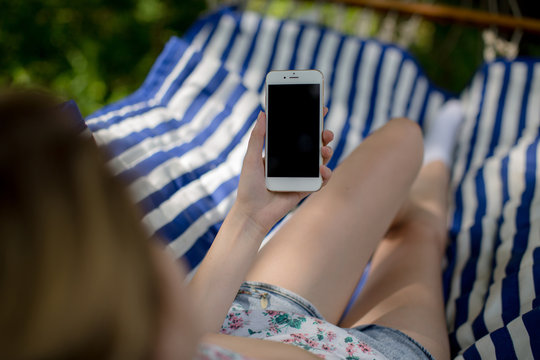 Young lady on hammock holding smartphone with blank screen