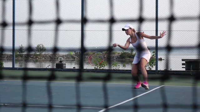 On the tennis court - personal trainer training a tennis player. Net in front. Dolly. Slow motion