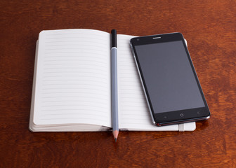 Opened notebook with a pencil and a smartphone, brown surface