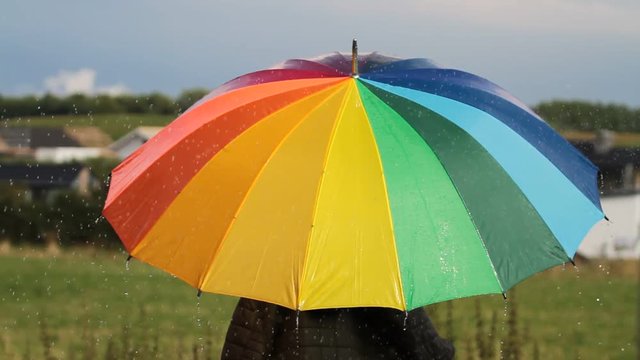 A person with rainbow colored umbrella in the rain