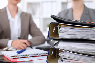 Binders with papers are waiting to be processed with businessman and secretary back in blur....