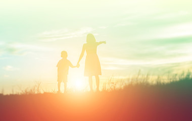 Mother encouraged her son outdoors at sunset, silhouette concept