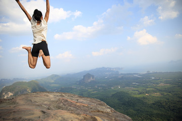 cheering young asian woman jumping on mountain peak rock..