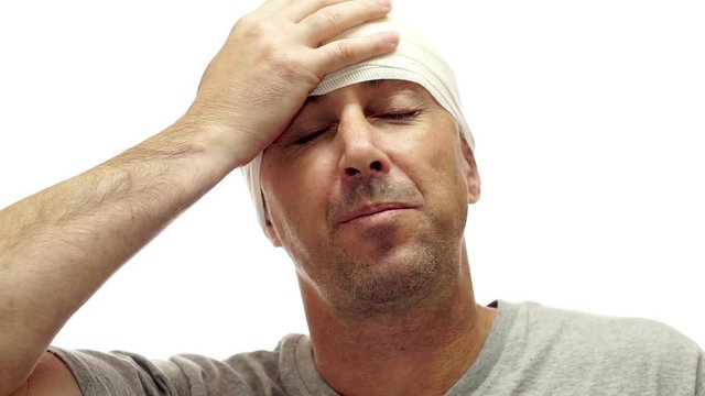 Male isolated on white with his head wrapped in a tensor bandage to sooth his pounding headache or migraine takes a pill to help relieve the pain.