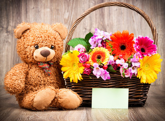 Beautiful flowers and a teddy bear on wooden background