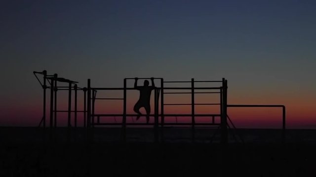 athlete pulls on the bar at sunset on the sea. silhouette