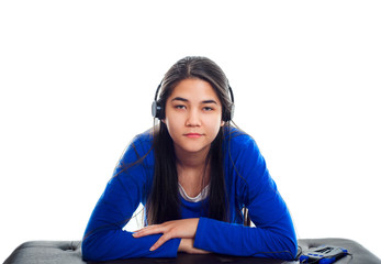 Biracial Asian, Caucasian teen girl in blue shirt listening to music on headphones while leaning on bench.