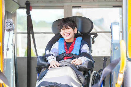Smiling disabled boy in wheelchair on yellow school bus lift