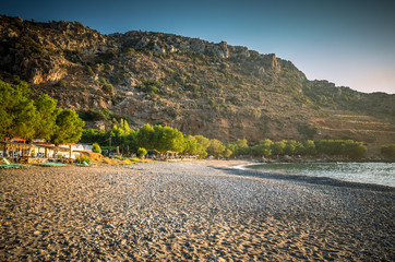 Sfinari Beach in Crete island, Greece. Straw parasols and sunbeds on the beach in twilight.