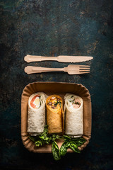 Vegetarian wraps in paper plate and wooden cutlery on dark background, top view, place for text. Healthy lunch