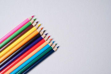 Colorful crayon pencils organized in a row over a grey background