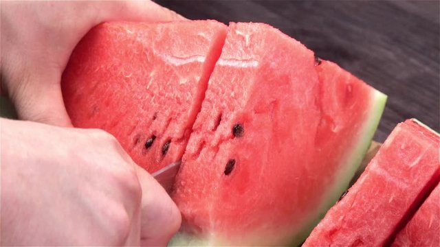 Man cuts red juicy ripe watermelon in slices with knife on dark background slowmotion. slow-motion pictures concept