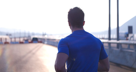 Attractive fit man running fast along big modern bridge at sunse